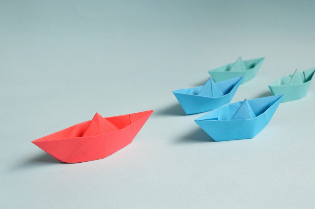 leader metaphor colored paper ships follow red paper ship